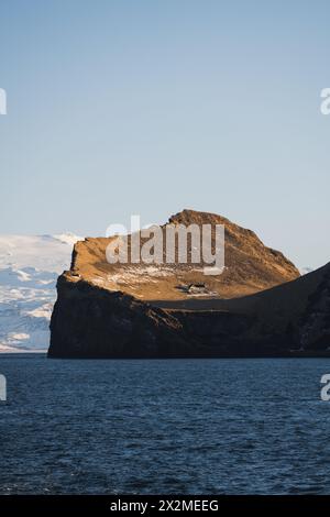 Ein einsames Haus steht am Rand einer dramatischen Klippe mit Blick auf den Ozean in Island, hervorgehoben durch das sanfte Abendlicht Stockfoto