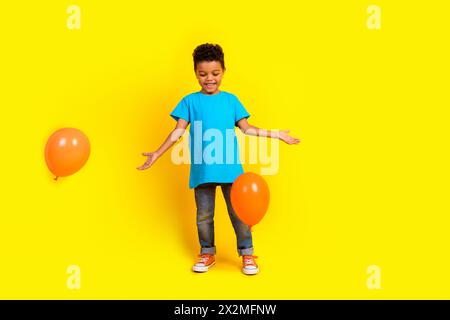 Ganzkörperfoto einer optimistischen, entzückenden, blauen T-Shirt-Jeans mit kleinen Kindern spielt mit Blasen, die auf leuchtendem gelbem Hintergrund isoliert sind Stockfoto