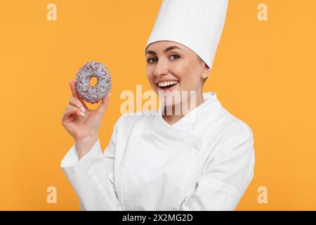 Glücklicher professioneller Konditor in Uniform mit köstlichem Donut auf gelbem Hintergrund Stockfoto