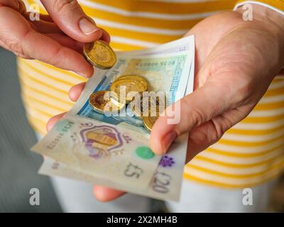 Nahaufnahme der Hände, die Bargeld in britischen Pfund-Banknoten und -Münzen auszahlen Stockfoto