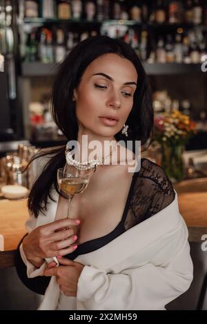 Eine anmutige Frau in einem fließenden weißen Gewand hält ein zartes Glas Wein in der Hand. Stockfoto