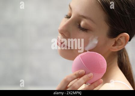 Junge Frau, die Gesicht mit Bürste und Reinigungsschaum auf hellem Hintergrund wäscht, Großaufnahme. Leerzeichen für Text Stockfoto