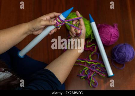 Nahaufnahme von lateinamerikanischen Frauenhänden, die eine Art von 25 mm geraden Kunststoffnadeln mit Fäden aus Wollmaterial verschiedener Farben halten. Konzept h Stockfoto