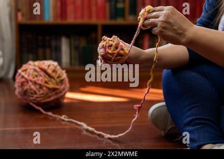 Nahaufnahme der Hände beim Abrollen eines Balls aus Wollfaser zum Stricken. Freizeit- und Freizeitkonzept Stockfoto