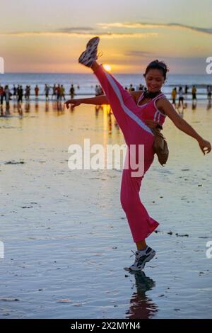 Eine junge indonesische Frau in Sportkleidung, die an einem belebten Strand von kuta bei Sonnenuntergang bali indonesia 2004 ihre „Keep fit“-Routine durchläuft Stockfoto