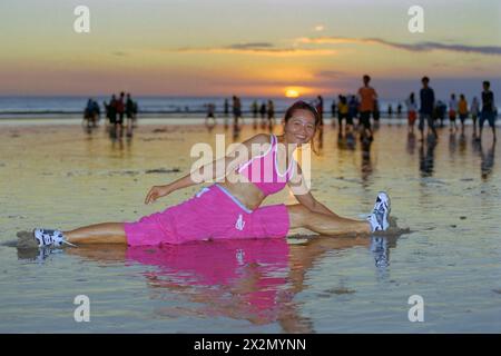 Eine junge indonesische Frau in Sportkleidung, die an einem belebten Strand von kuta bei Sonnenuntergang bali indonesia 2004 ihre „Keep fit“-Routine durchläuft Stockfoto