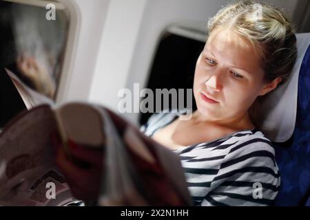 Junge schöne Frau in gestreiftem T-Shirt liest Zeitschrift im Flugzeug. Stockfoto