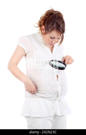 Schwangere Frau in weiß schaut durch die Lupe auf den Bauch isoliert auf weißem Hintergrund. Stockfoto