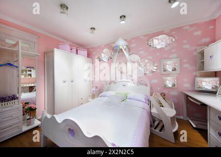 Stilvolles rosafarbenes Schlafzimmer für Mädchen mit weißem Kleiderschrank, großem Bett und Computerschreibtisch. Stockfoto