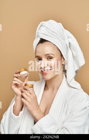 Eine umwerfende Frau in einem weißen Gewand hält Creme mit einem Look der Nachsicht und des Genusses. Stockfoto