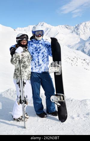 Paare in Sportanzügen und Helmen stehen mit Snowboard und Skiern auf dem Berg. Stockfoto