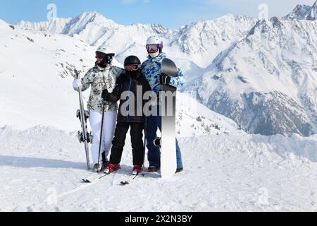 Familie in Helmen steht mit Snowboard und Skiern am sonnigen Tag am Berg. Stockfoto