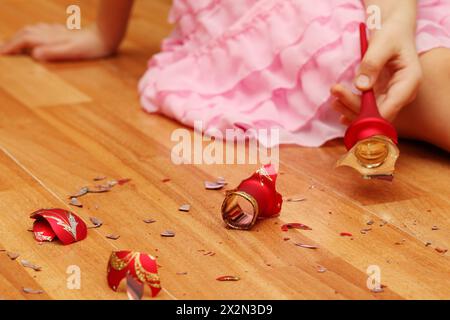 Hände eines kleinen Mädchens in rosafarbenem Kleid, das auf dem Boden geschmiedete Weihnachtskugeln aufnimmt. Stockfoto