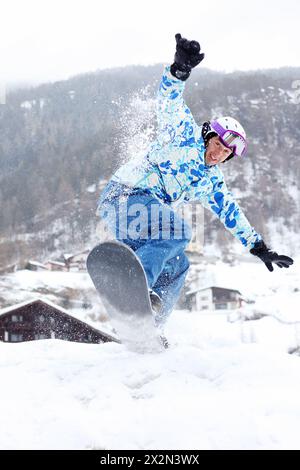 Lächelnder Snowboarder springt im verschneiten Winter auf dem Berg auf das Snowboard. Stockfoto