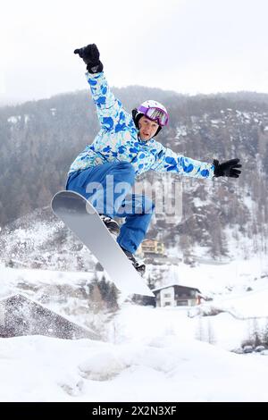 Snowboarder in Helm und Sportanzügen springt im verschneiten Winter auf dem Snowboard in den Bergen. Stockfoto