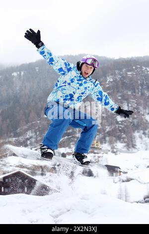 Schreiender Snowboarder in Helm und Sportanzug springt im verschneiten Winter auf dem Snowboard auf den Bergen. Stockfoto