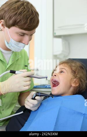 Junger Zahnarzt hält Speichel-Saug- und Schleifbohrer, Happy Girl öffnet ihren Mund in der Zahnklinik. Stockfoto