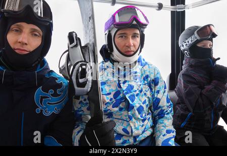 Drei Skifahrer mit Helmen fahren mit der Seilbahn in den Bergen. Konzentrieren Sie sich auf den Mittelsmann. Stockfoto