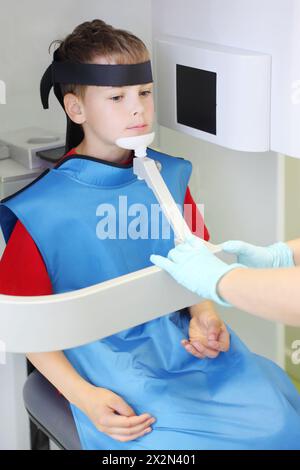 Zahnarzthände bereiten das Tragen des Jungen in schützender Bleischürze zum Kieferröntgenbild in der Zahnklinik vor. Konzentrieren Sie sich auf den Patienten. Stockfoto