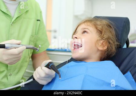 Zahnarzthände halten Speichel-Saug- und Schleifbohrer, Happy Girl öffnet ihren Mund in der Zahnklinik. Stockfoto