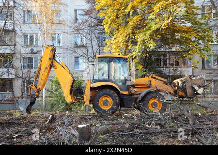 Großer gelber Planierraupen entfernt im Herbst gefällte Bäume in der Nähe des Wohngebäudes. Stockfoto