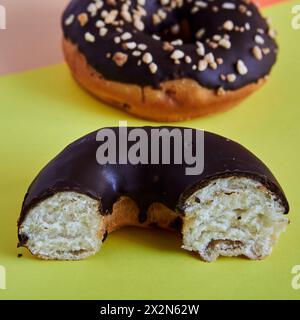 Ein halber, mit Schokolade überzogener Donut auf grünem Hintergrund, ein ganzer Donut im Hintergrund ist unscharf. Quadratisches Format. Stockfoto