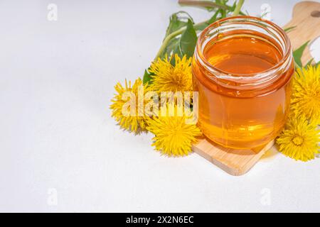 Löwenzahnmarmelade, Gelee-Konfitüre in einem Glas mit frischen Löwenzahnblüten auf weißem Tischhintergrund Stockfoto