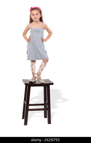 Kleines Mädchen im gestreiften Kleid steht auf dem Hocker Stockfoto