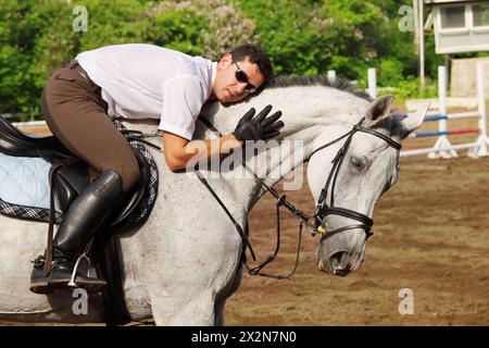 Jockey in Brille umarmt Pferd auf hippodrom Stockfoto