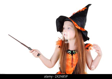 Kleines Mädchen in orangefarbenem Hexenkostüm für Halloween hält Zauberstab und Zauber isoliert auf weißem Hintergrund. Stockfoto