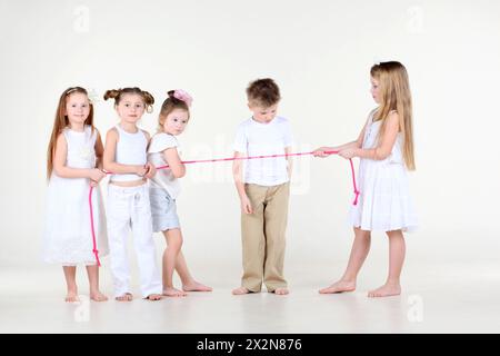Vier kleine Mädchen in weißer Kleidung ziehen über rosa Seil und der Junge schaut sich das Seil an. Stockfoto
