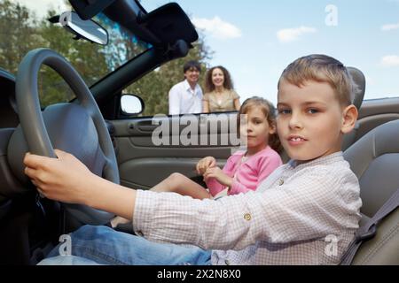 Сlose-up Junge sitzt am Lenkrad des Cabriolets, seine Schwester sitzt auf einem Beifahrersitz Stockfoto