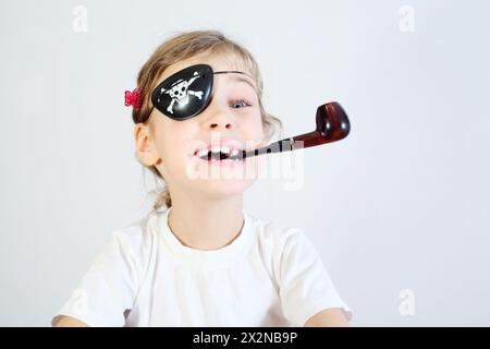 Das kleine glückliche Mädchen in weiß mit pipetischem und verbundenem Auge ist Piratin. Stockfoto