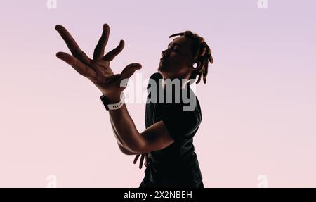 Ausdrucksstarker junger Mann mit Dreadlocks tanzt energetisch im Studio zum Rhythmus eines Liedes. Seine Augen geschlossen, die Hände in Bewegung, er hört mit einem Funken zu Stockfoto