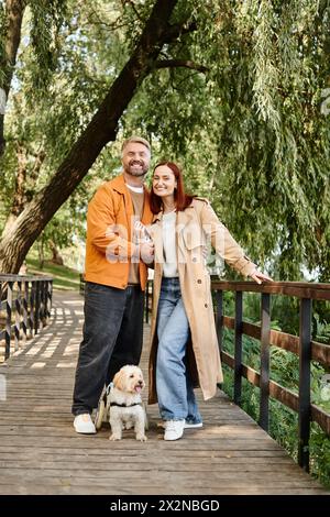Erwachsenes Paar in lässiger Kleidung, das mit seinem geliebten Hund auf einer Brücke steht. Stockfoto