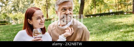 Ein Mann und eine Frau in lässiger Kleidung, die Weingläser in der Hand halten und einen romantischen Spaziergang im Park genießen. Stockfoto