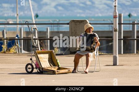 Eine Strassenmusikerin sitzt mit ihrem Handeorgel an der Uferpromenade in Friedrichshafen und spielt Musik. (Friedrichshafen, Deutschland, 21.08.2022) Stockfoto