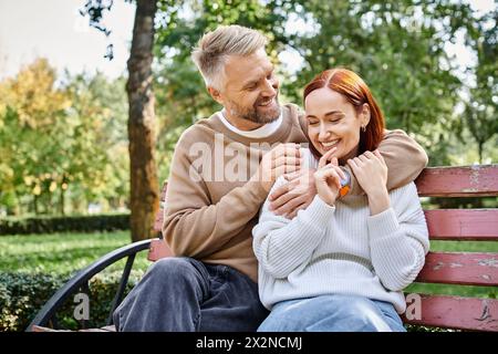 Erwachsenes Paar in legeren Kleidern, das sich auf einer Parkbank entspannt. Stockfoto