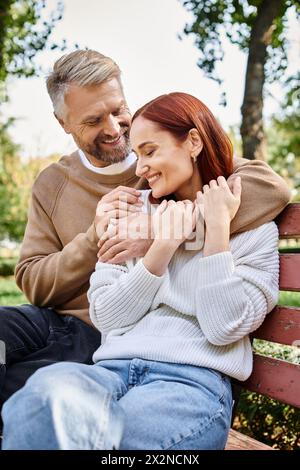 Ein liebevolles Paar in lässiger Kleidung, das zusammen auf einer Holzbank in einer ruhigen Parklandschaft sitzt. Stockfoto