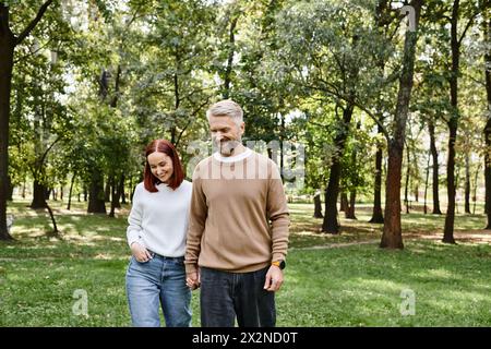 Erwachsenes Paar in lässiger Kleidung, das einen gemütlichen Spaziergang durch einen ruhigen Park macht. Stockfoto