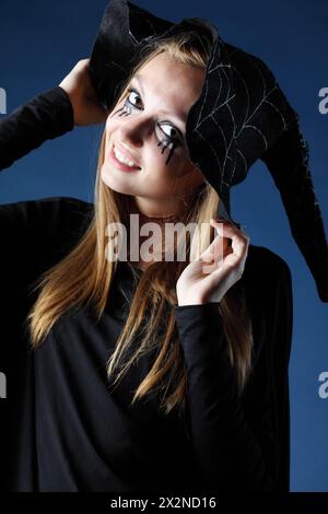 Lächelndes Zombie-Mädchen mit schwarzen Tränen und durchgeschnittener Kehle in großem schwarzen Hut. Stockfoto