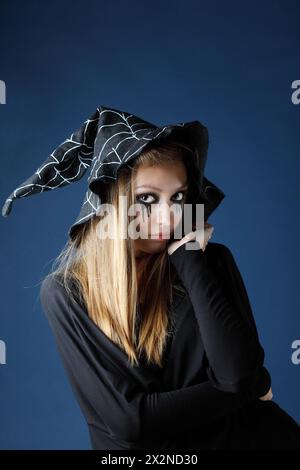 Hübsches Zombie-Mädchen mit schwarzen Tränen und durchgeschnittener Kehle in großem schwarzen Hut. Stockfoto