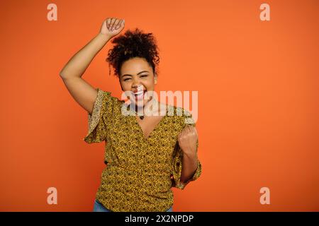 Die schöne afroamerikanische Frau in stilvoller Kleidung hebt ihre Arme vor einer lebendigen Kulisse freudig in die Luft. Stockfoto