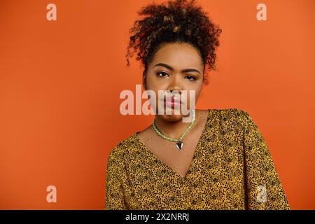 Die atemberaubende Afroamerikanerin mit Halskette posiert vor einem leuchtenden orangefarbenen Hintergrund. Stockfoto