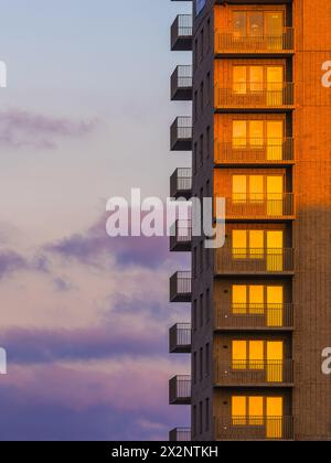 Die untergehende Sonne strahlt ein warmes Leuchten auf die Backsteinfassade eines Wohnhochhauses in Göteborg, Schweden. Auf einer Seite säumen Balkone, die einen Blick auf das Hotel bieten Stockfoto