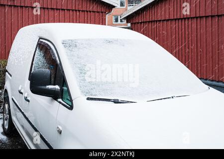 Ein weißer Van parkt vor einem roten Gebäude in Schweden. Die Szene zeigt urbane Architektur mit schneebedeckter Umgebung. Stockfoto