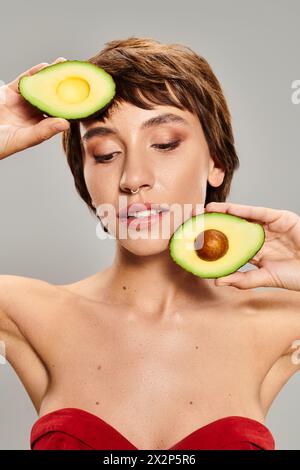 Die junge Frau hält eine Avocado spielerisch vor einem lebendigen Hintergrund ins Gesicht. Stockfoto