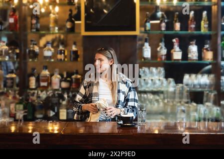 Die Kellnerin stand in der Bar und wischte und polierte das Bierglas. Die Barkeeperin arbeitet an der Bar, bereitet und putzt, arbeitet, bevor Gäste kommen, Stockfoto