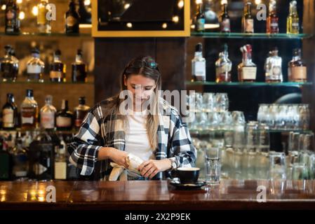 Die Kellnerin stand in der Bar und wischte und polierte das Bierglas. Die Barkeeperin arbeitet an der Bar, bereitet und putzt, arbeitet, bevor Gäste kommen, Stockfoto