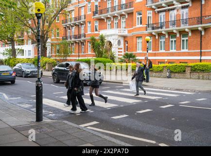 Drei junge Frauen, gefolgt von einer reiferen Dame, die auf dem Handy Selfie macht, überqueren den Zebraübergang der Abbey Road. St John's Wood London England UK Stockfoto